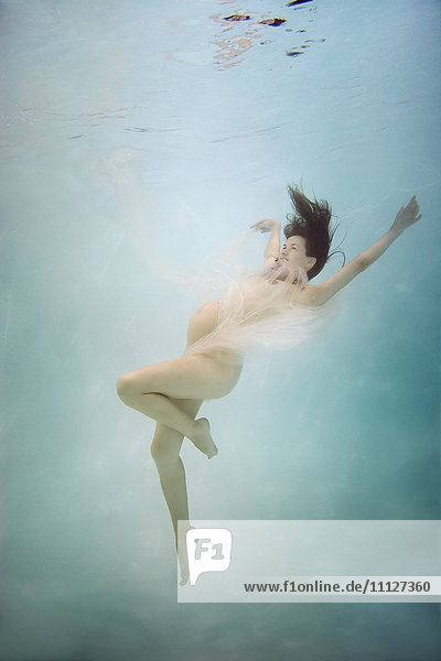 Schwangere kaukasische Frau schwimmt unter Wasser
