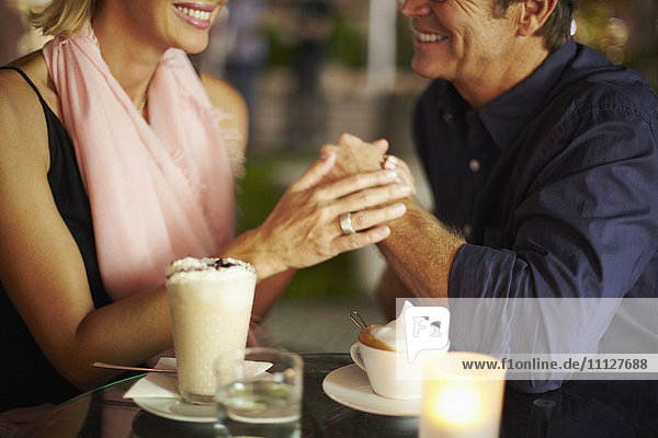 Paar hält sich bei einem Kaffee im Restaurant an den Händen