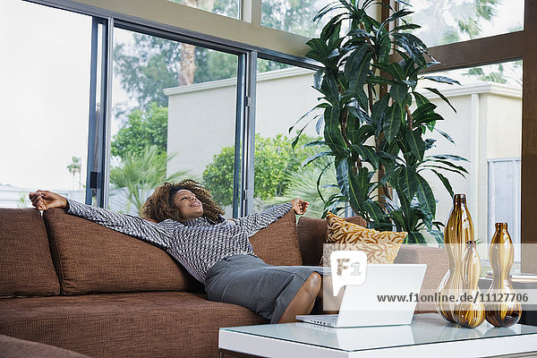 Afrikanische Frau entspannt auf Sofa in modernem Wohnzimmer