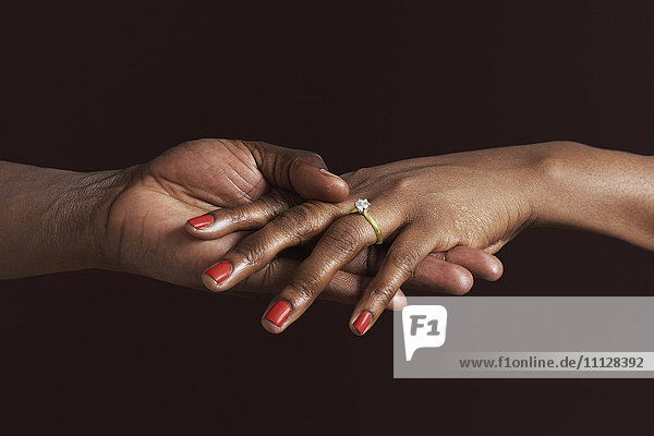 African woman with engagement ring holding fiancee's hand