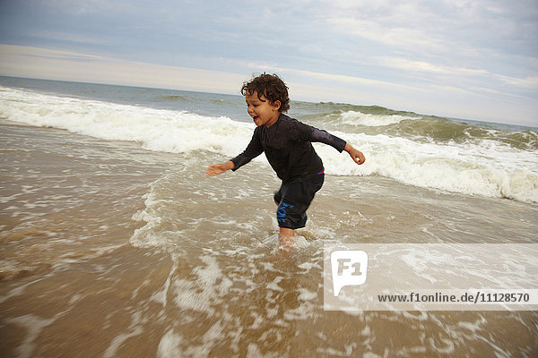 Gemischtrassiger Junge spielt in den Wellen des Ozeans