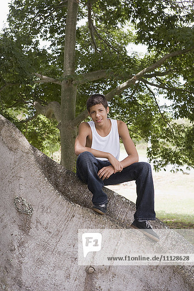 Hispanic teenager sitting on large tree trunk