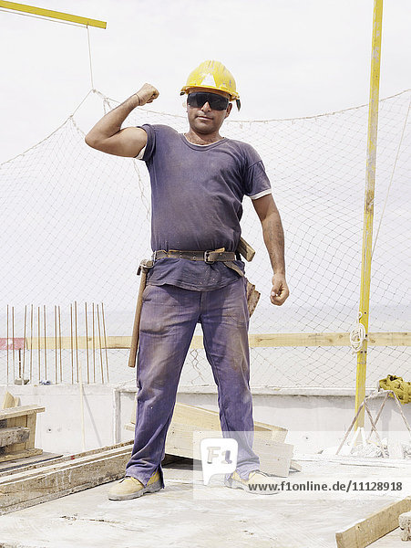 Hispanischer Arbeiter  der auf einer Baustelle seinen Bizeps beugt