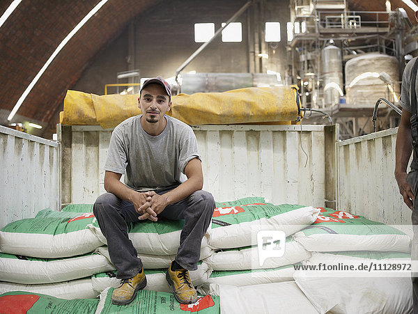 Hispanic worker sitting on bag in factory