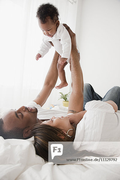 African couple holding baby up in bed