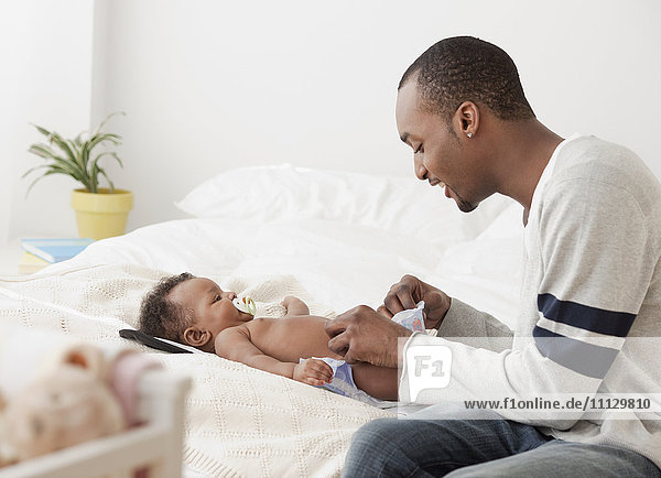 Afrikanischer Mann wechselt die Windel eines Babys im Bett