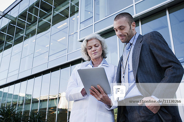 Arzt und Geschäftsmann benutzen digitales Tablet im Freien