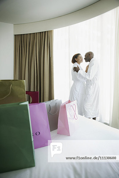 Couple kissing in bathrobes with shopping bags on bed