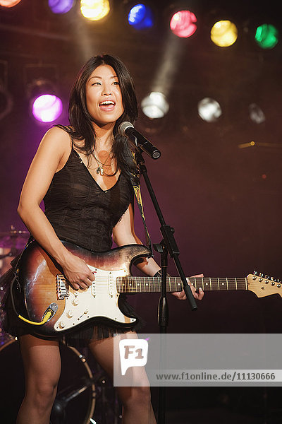 Asian woman singing and playing electric guitar onstage