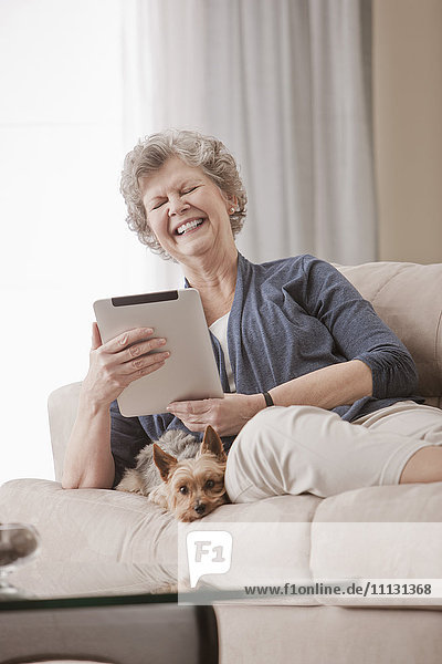 Caucasian woman sitting on sofa using digital tablet with dog
