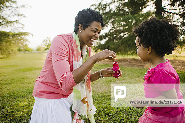 Schwarze Mutter und Tochter beim Blasen von Seifenblasen im Park