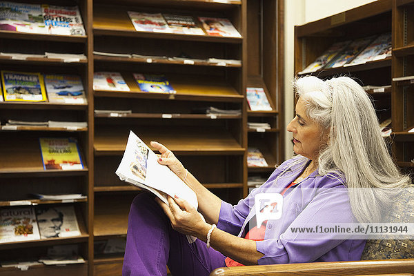 Ältere hispanische Frau liest in der Bibliothek Zeitung