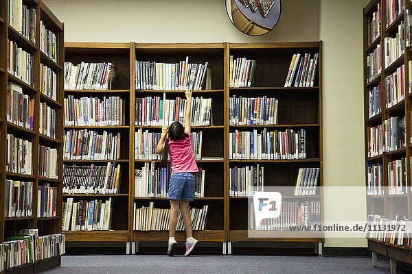 Girl reaching for book on library shelf