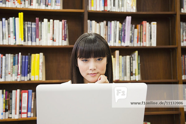 Asiatische Frau benutzt Laptop in einer Bibliothek