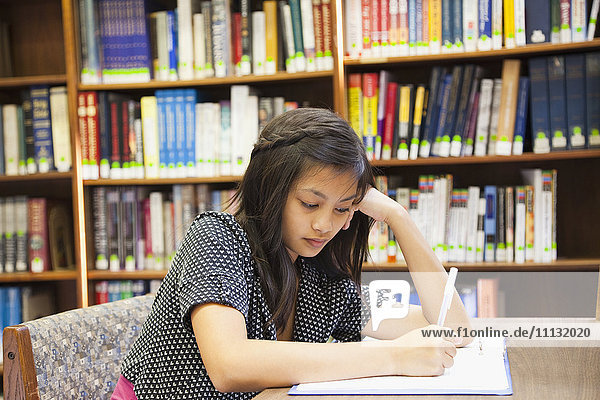 Asian girl doing homework in library