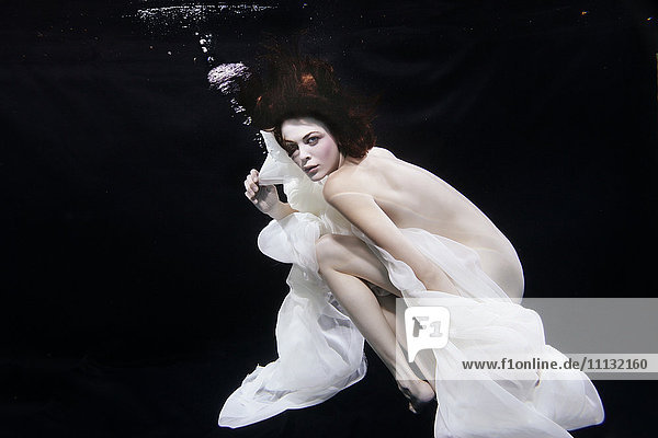 Gemischtrassige Frau mit Kopftuch schwimmt unter Wasser