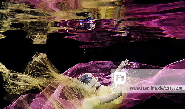 Kaukasische Frau mit Kopftuch schwimmt unter Wasser