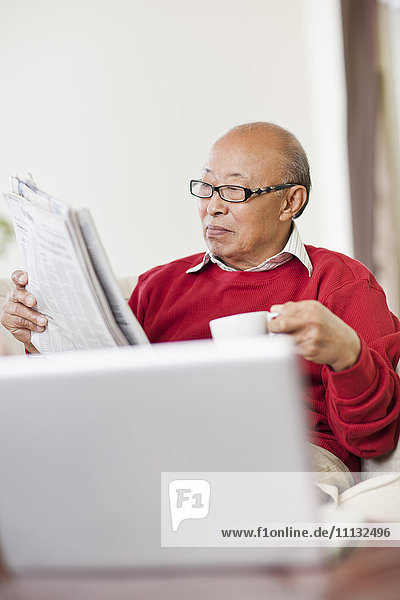 Chinesischer Mann liest Zeitung und trinkt Kaffee