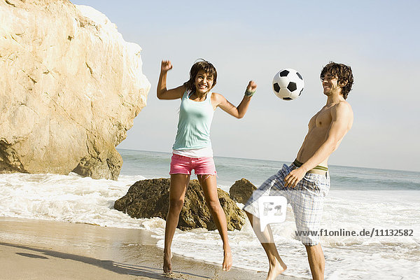 Pärchen spielt mit Fußball am Strand