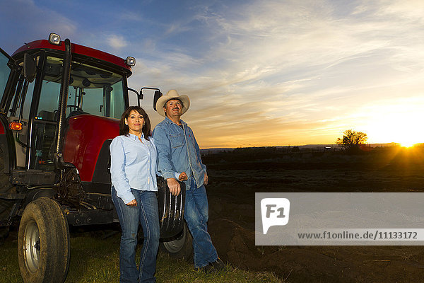 Hispanisches Paar steht neben Traktor auf Bauernhof
