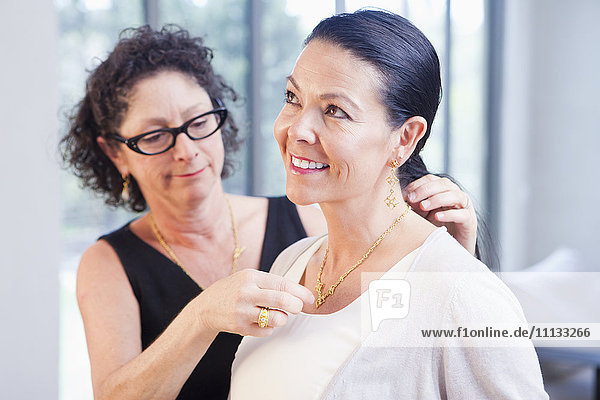 Frau hilft Kundin beim Anlegen einer Halskette in einem Juweliergeschäft