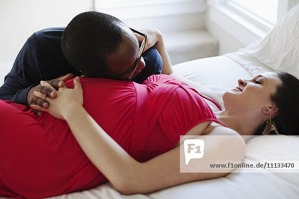 Ehemann liegt mit schwangerer Frau auf dem Bett