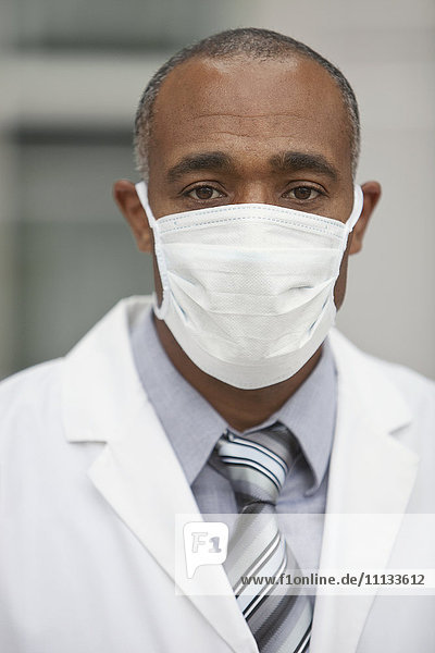 Gemischtrassiger Arzt mit chirurgischer Maske