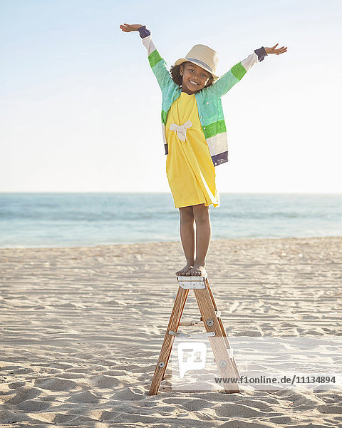 Gemischtrassiges Mädchen steht auf einer Leiter am Strand