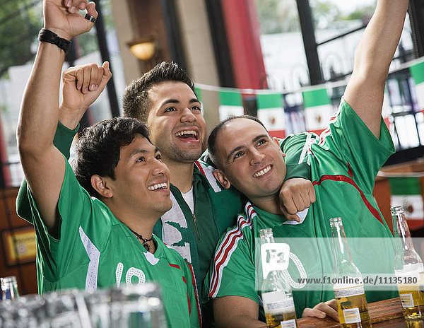 Jubelnde hispanische Männer beim Fernsehen in einer Sportbar