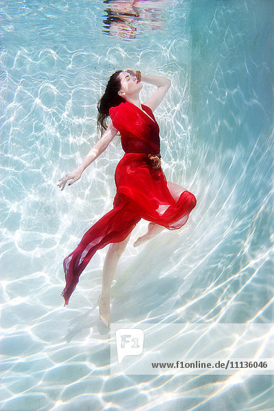 Gemischtrassige Frau im Kleid unter Wasser im Schwimmbad