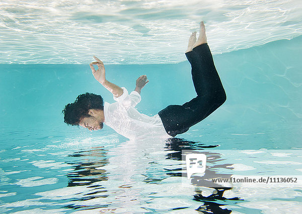 Gemischtrassiger Mann in Kleidung unter Wasser im Schwimmbad