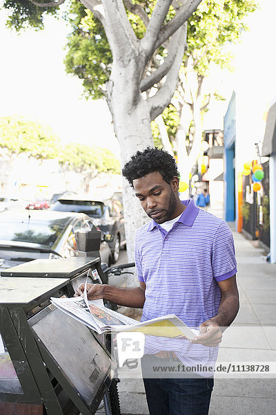 Afroamerikanischer Mann liest Zeitung auf dem Bürgersteig