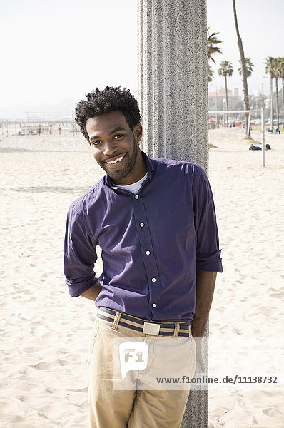 Afroamerikanischer Mann lehnt sich am Strand an eine Stange