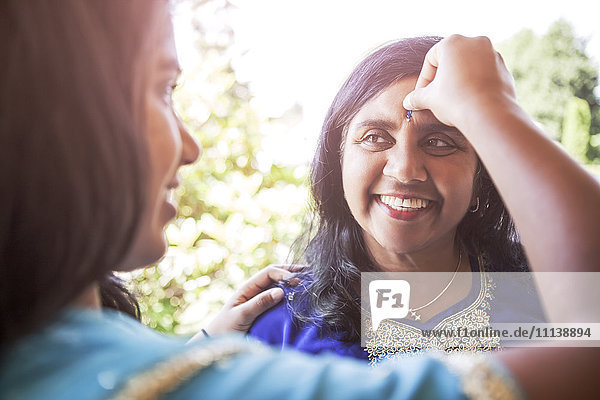 Indische Frau legt Schmuckstück auf die Stirn ihrer Mutter