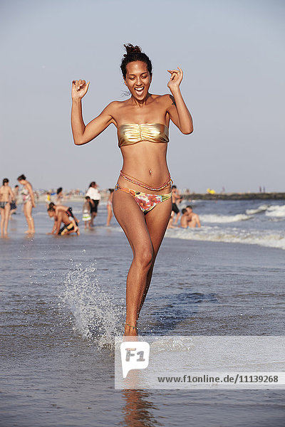Gemischtrassige Frau watet am Strand im Meer