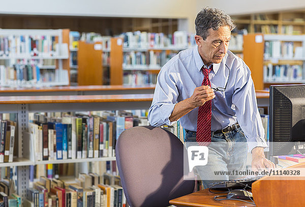 Älterer Mann arbeitet am Computer in einer Bibliothek