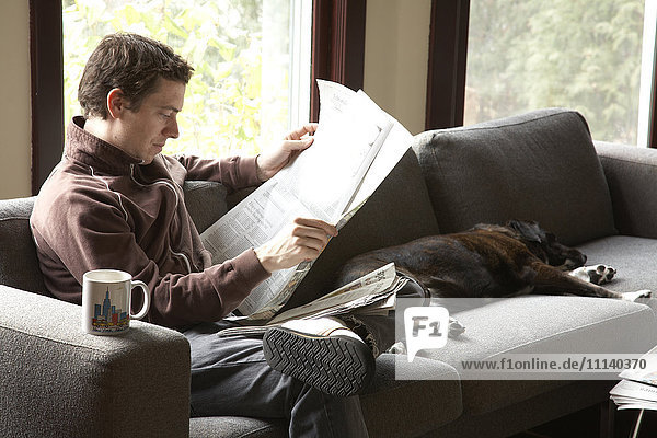 Kaukasischer Mann liest Zeitung auf Sofa mit Hund