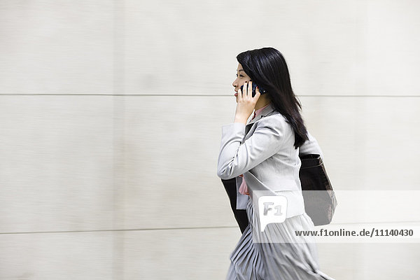 Chinesische Geschäftsfrau  die spazieren geht und mit einem Handy telefoniert