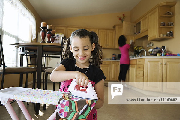 Mädchen mit Spielzeugbügeleisen und Bügelbrett in der Küche