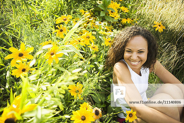 Lächelnde hispanische Frau in einem Blumenfeld sitzend