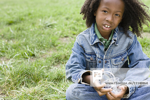 Afroamerikanischer Junge sitzt im Gras und hält ein Glas
