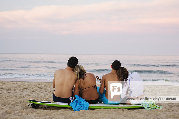 Teenager-Pärchen sitzt auf einem Surfbrett am Strand