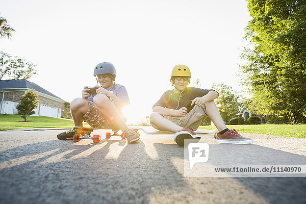 Weiße Jungen sitzen auf Skateboards und benutzen Handys