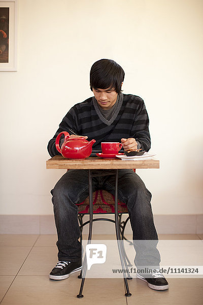 Gemischtrassiger Mann trinkt Tee und benutzt ein digitales Tablet in einem Café