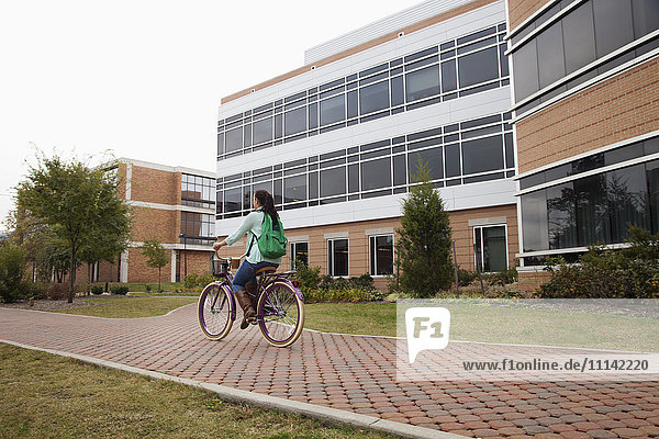 Kaukasischer Student fährt mit dem Fahrrad auf dem Campus