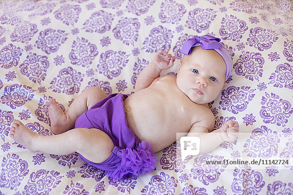 Baby Mädchen trägt lila Windel und Stirnband auf Decke