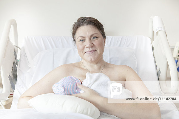 Kaukasische Mutter  die ihre neugeborene Tochter im Krankenhausbett stillt