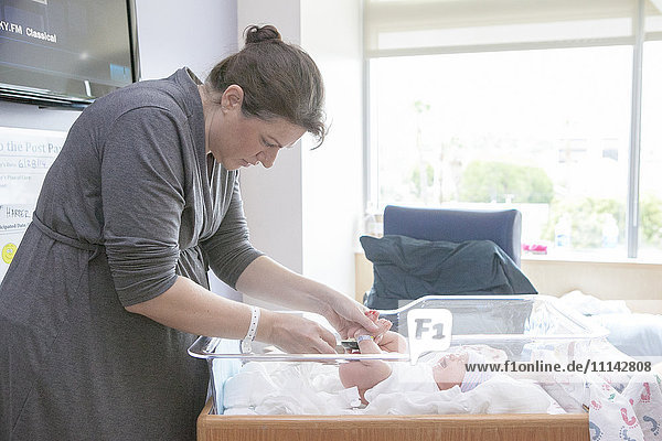 Kaukasische Mutter wickelt ihre neugeborene Tochter im Krankenhausbettchen