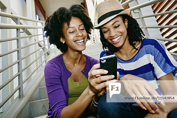 Women using cell phone together on steps