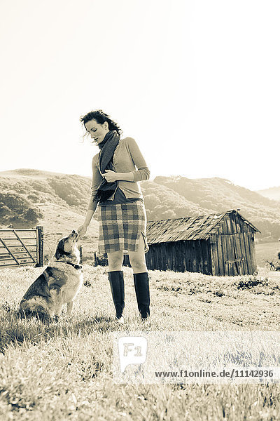 Frau streichelt Hund in ländlicher Landschaft